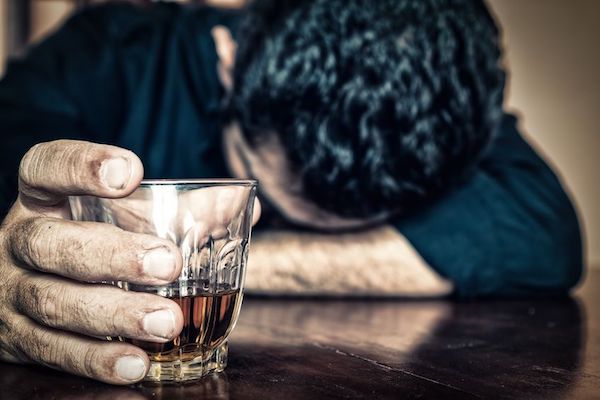 A despondent man holding a drink with his head down