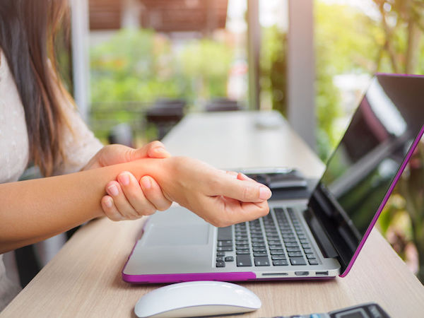 A woman at a laptop, holding her wrist in pain