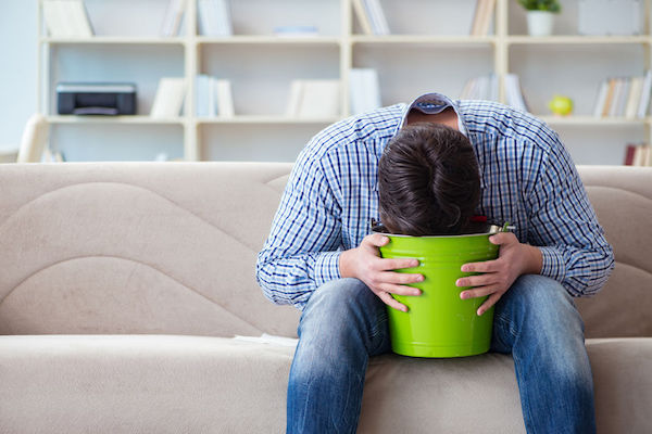A man sitting on the couch with his head in a bucket