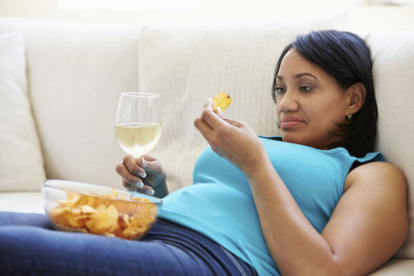 A woman sitting on the couch with wine and chips