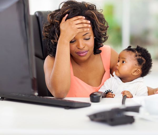 A woman holding her head at her desk with her baby